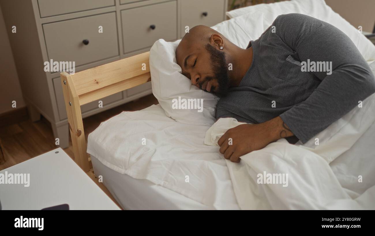 Hübscher junger afroamerikaner mit Bart, der friedlich im Bett in einem gemütlichen Schlafzimmer schläft Stockfoto