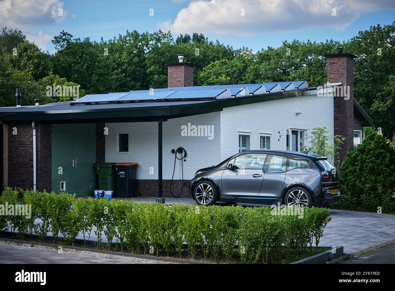 Ein Elektrofahrzeug mit Ladegerät in einem Wohnhaus mit Solarpaneelen. Ein modernes Beispiel für nachhaltiges Wohnen und erneuerbare Energien Stockfoto