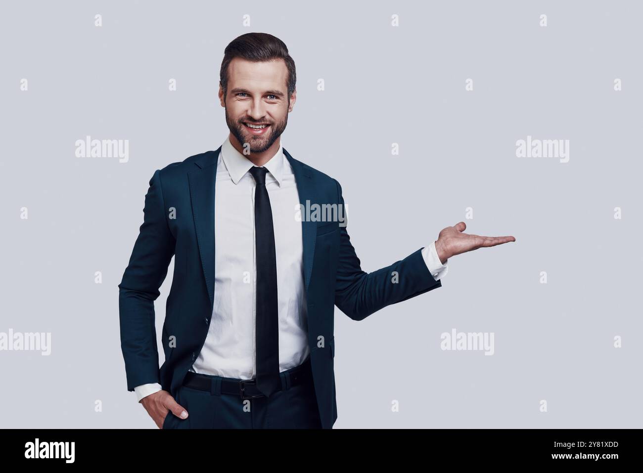 Sehen Sie es sich an! Hübscher junger Mann, der auf den Kopierraum zeigt und lächelt, während er vor grauem Hintergrund steht Stockfoto