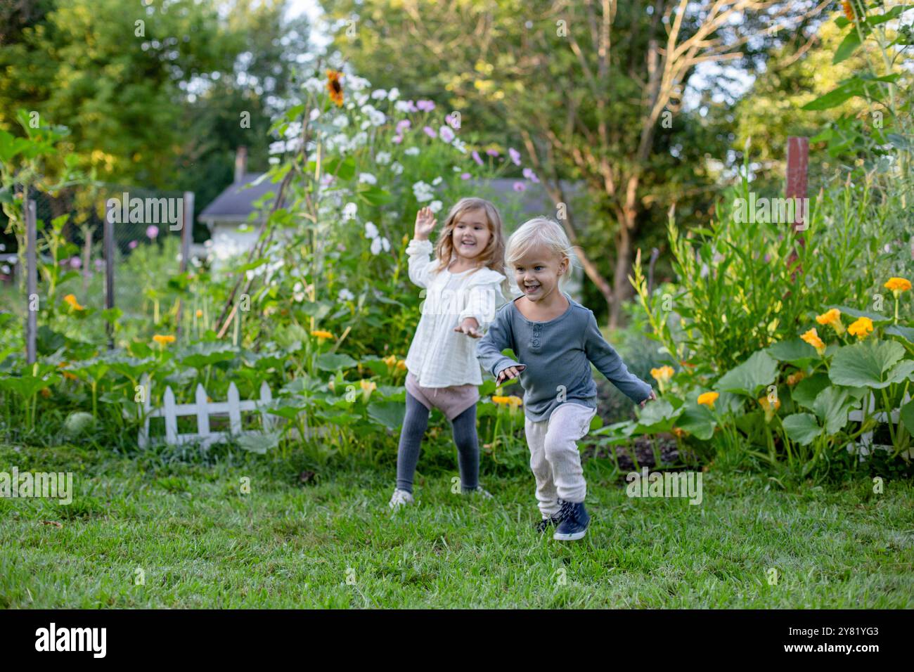 Zwei glückliche Kinder laufen Hand in Hand durch einen üppigen Garten voller Blumen und Pflanzen. Stockfoto