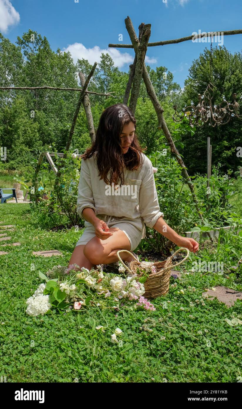 Frau im Garten, die an einem sonnigen Tag frisch gepflückte Blumen in einen Korb legt. Stockfoto