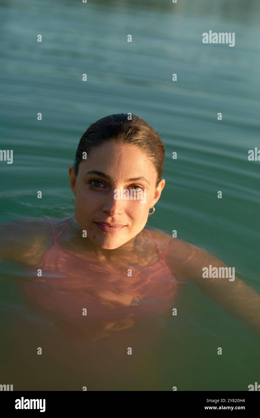 Frau, die in einem Gewässer mit zurückgezogenem Haar und Sonnenlicht, das ihr Gesicht hervorhebt, badete. Stockfoto