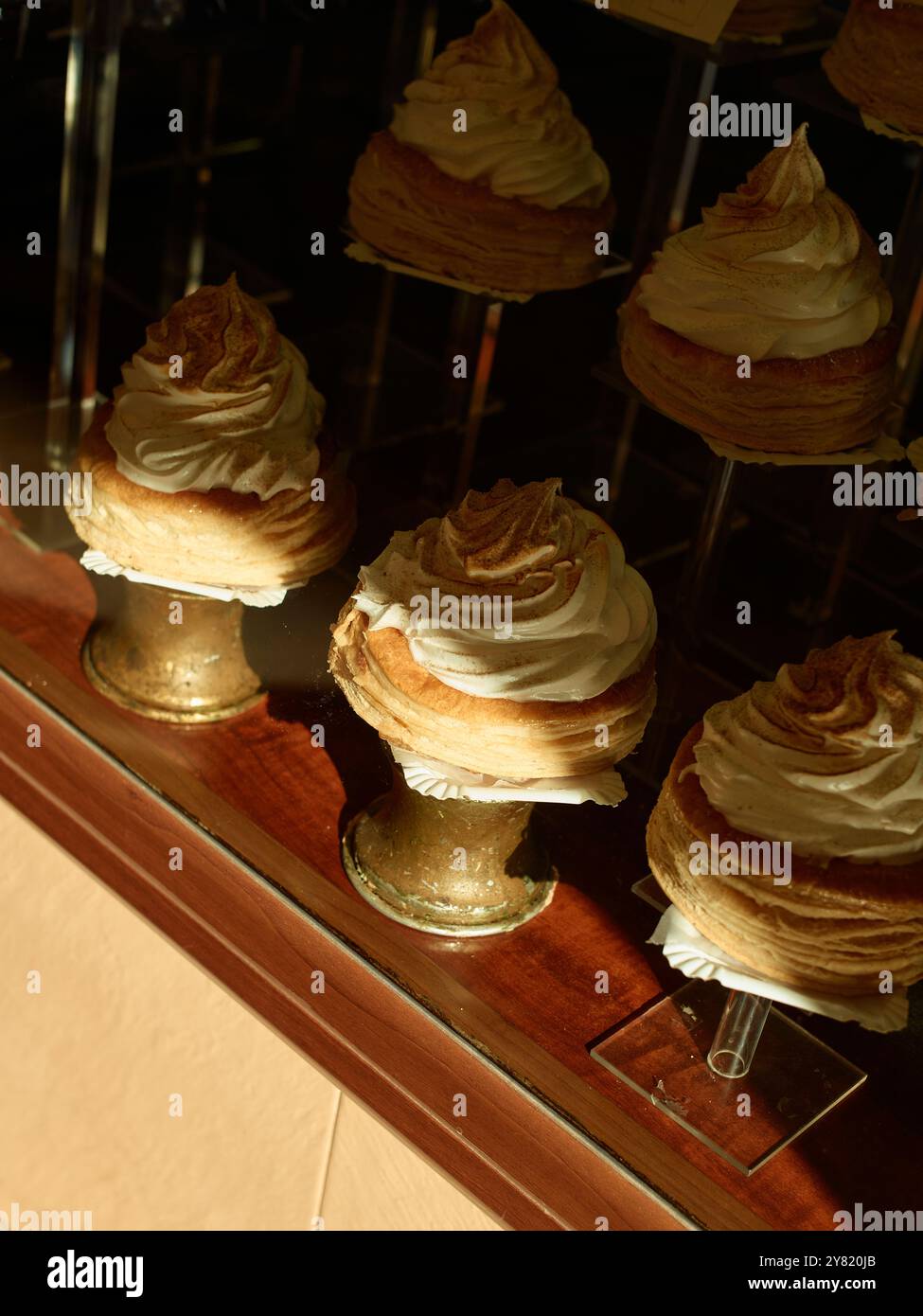 Gourmet-Meringue-Gebäck auf eleganten Metallständern in einem Bäckereifenster unter warmer Beleuchtung. Stockfoto