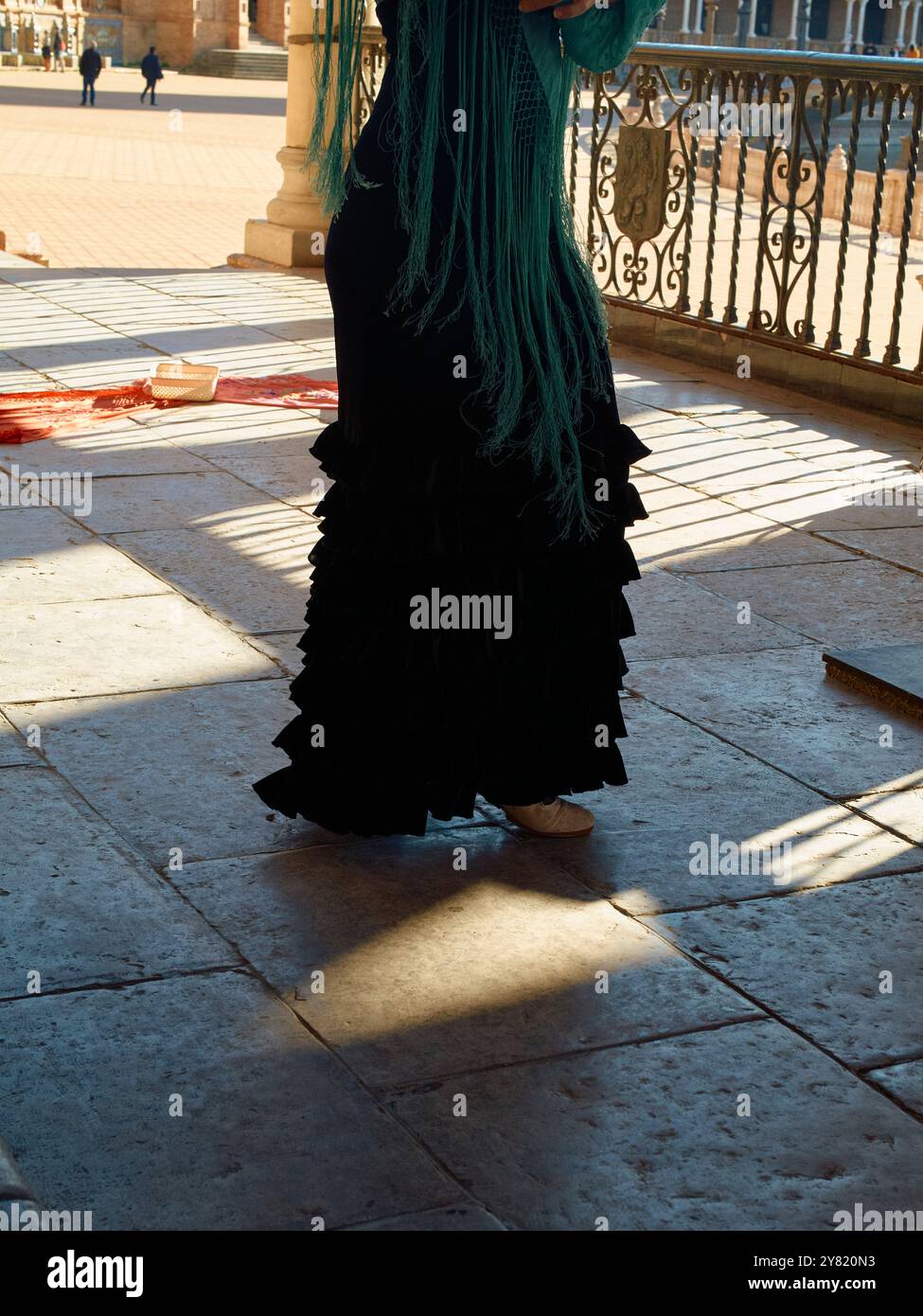 Frau mit langen grünen Haaren steht auf einer sonnendurchfluteten Terrasse mit Schatten auf dem Boden. Stockfoto