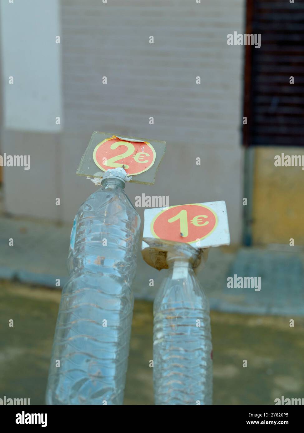Zwei Plastikflaschen mit Preisanhänger oben, eine mit 1 Euro und die andere mit 2 Euro, vor einem verschwommenen urbanen Hintergrund. Stockfoto