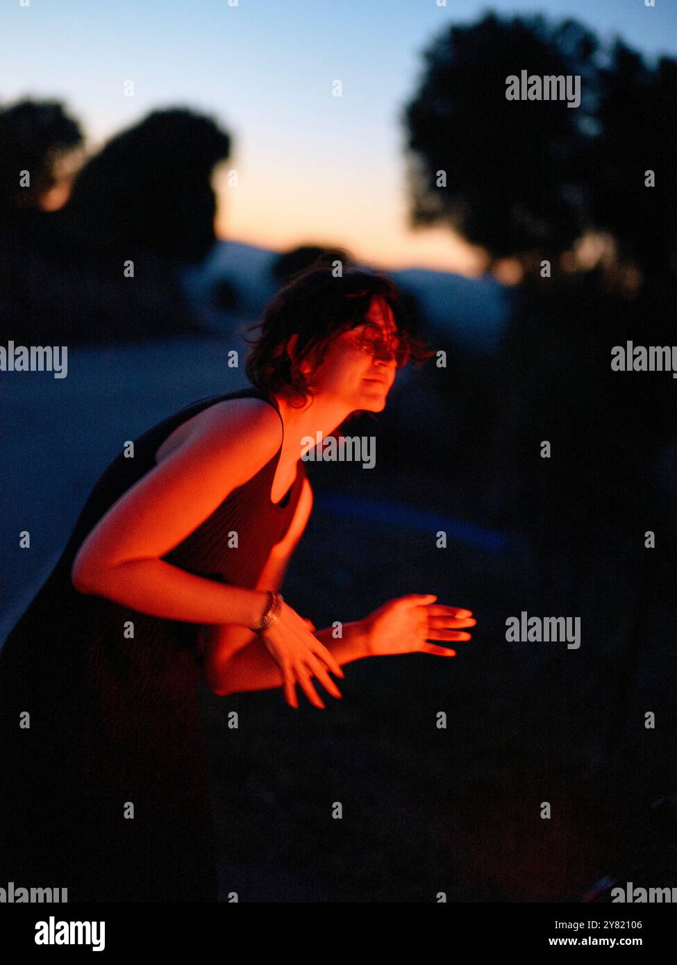 Silhouettenfrau, die sich in der Dämmerung auf einer ruhigen Straße mit einem nachdenklichen Ausdruck nach vorne lehnt. Stockfoto