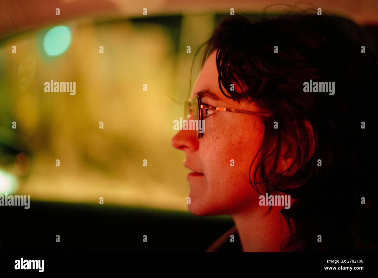 Seitenprofil eines lächelnden jungen Erwachsenen mit Brille in einem schwach beleuchteten Autoinnenraum bei Nacht. Stockfoto