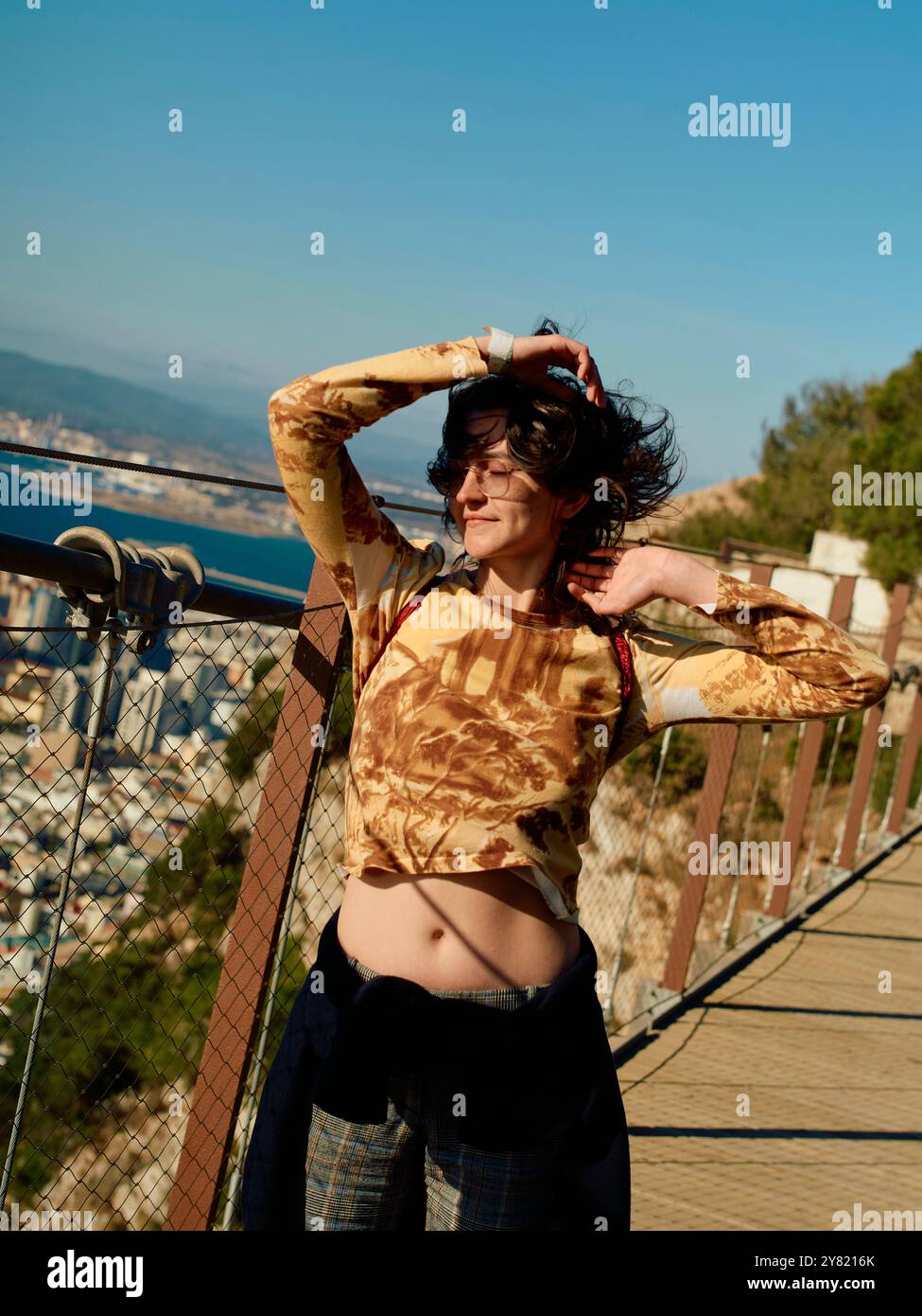 Frau genießt den Sonnenschein auf einem malerischen Ausblick mit einem Hintergrund aus klarem Himmel und fernen Landschaften. Stockfoto