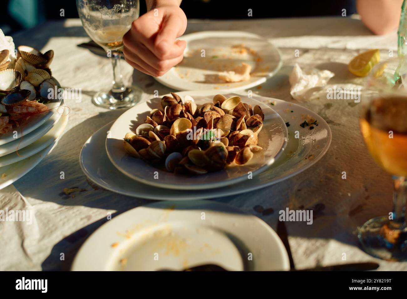 Eine Nahaufnahme eines Tisches während einer Meeresfrüchtemahlzeit mit einem Teller Muscheln, teilweise gegessen Speisen und Getränken unter warmer Beleuchtung. Stockfoto