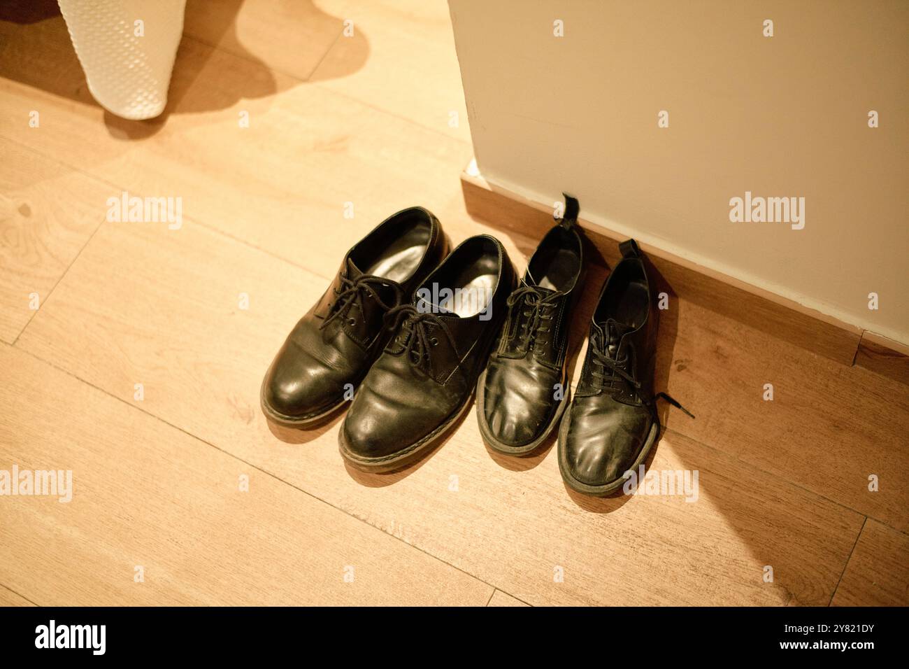 Ein Paar schwarze Lederschuhe, ordentlich auf einem Holzboden neben einer weißen Wand platziert. Stockfoto