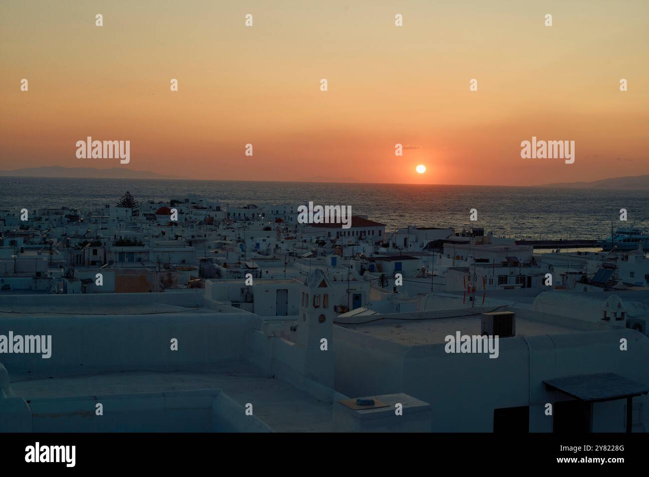 Sonnenuntergang über einer traditionellen, weiß getünchten Stadt, während die Sonne unter dem Horizont eintaucht und ein warmes Leuchten erzeugt. Stockfoto