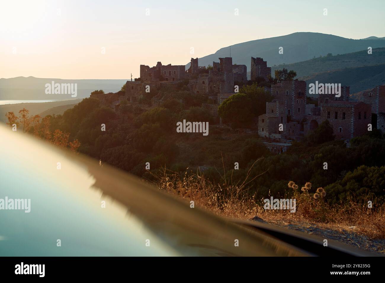 Das Licht am frühen Morgen taucht ein verlassenes Steindorf mit einer Kulisse aus sanften Hügeln und einem ruhigen See auf. Stockfoto