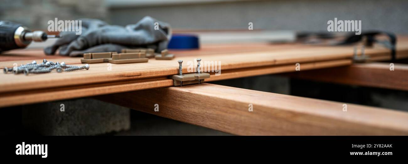 Eine detaillierte Ansicht des Montageprozesses für Decks mit Schwerpunkt auf versteckten Befestigungselementen und Schrauben, die zur Befestigung von Holzdielen verwendet werden. Eine Bohrmaschine, Sre Stockfoto