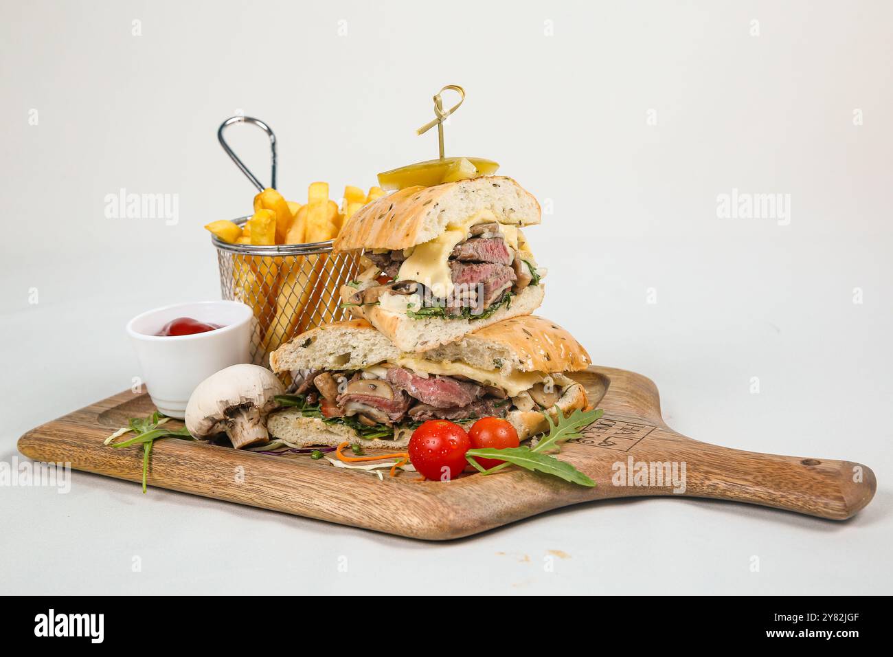 Rindersteak-Sandwich mit Rucola, Tomate und Parmesan auf einem Schneidebrett. Weißer Hintergrund. Stockfoto