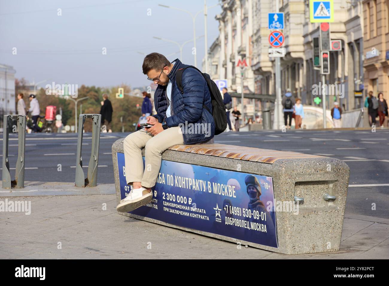 Mann, der auf der Stadtbank sitzt, mit einem Banner und einem Aufruf zum Vertragsdienst in der russischen Armee Stockfoto