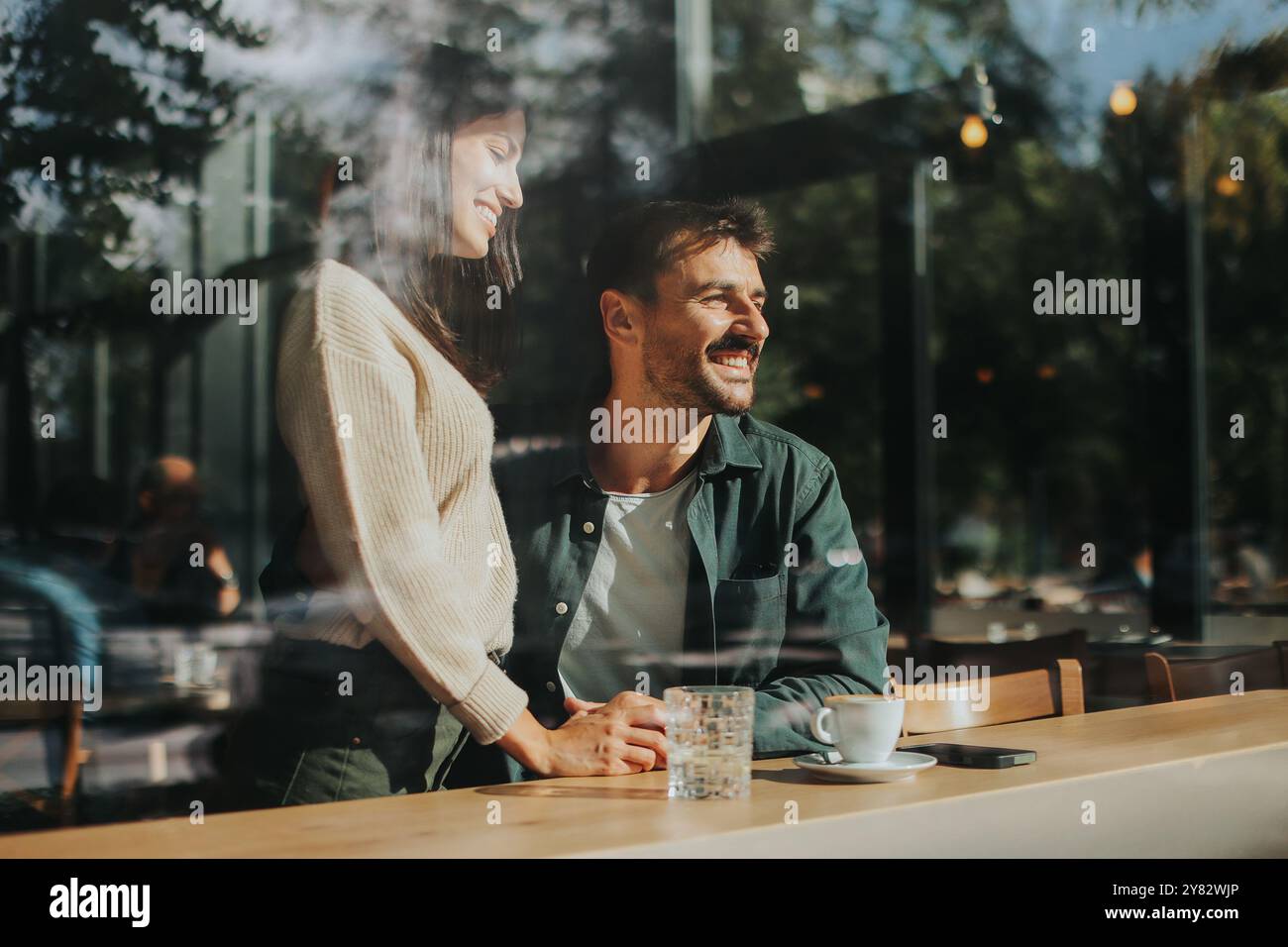 Zwei Freunde teilen sich Lachen und warme Drinks in einem charmanten Café und schaffen eine einladende Atmosphäre, die an einem sonnigen Tag die Verbindung und Freude feiert Stockfoto