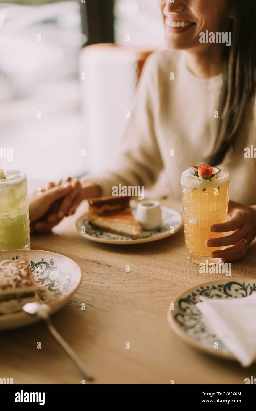 Eine Frau lächelt, während sie ein buntes Getränk hält, umgeben von köstlichem Essen. Freunde teilen Lachen und gemütliche Momente in einem charmanten Café während einer Leisu Stockfoto