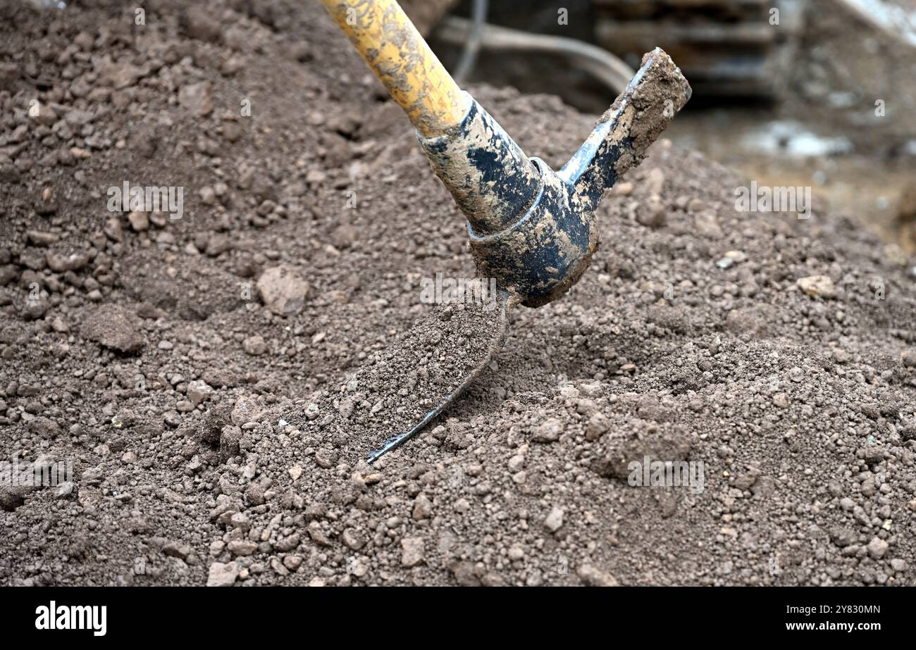 Mattock wird verwendet, um Boden von einer Bohrstelle der Schnecke zu bewegen Stockfoto