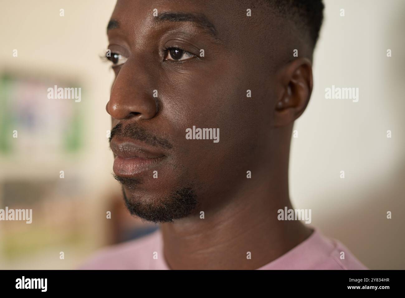 Nahaufnahme eines jungen Afrikaners, der allein zu Hause steht und tief in Gedanken schaut Stockfoto