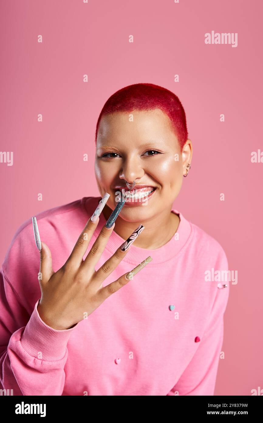 Eine selbstbewusste junge Frau mit pinkfarbenen Haaren und Nasenpiercing zeigt ihren auffälligen Stil in einem Studio. Stockfoto