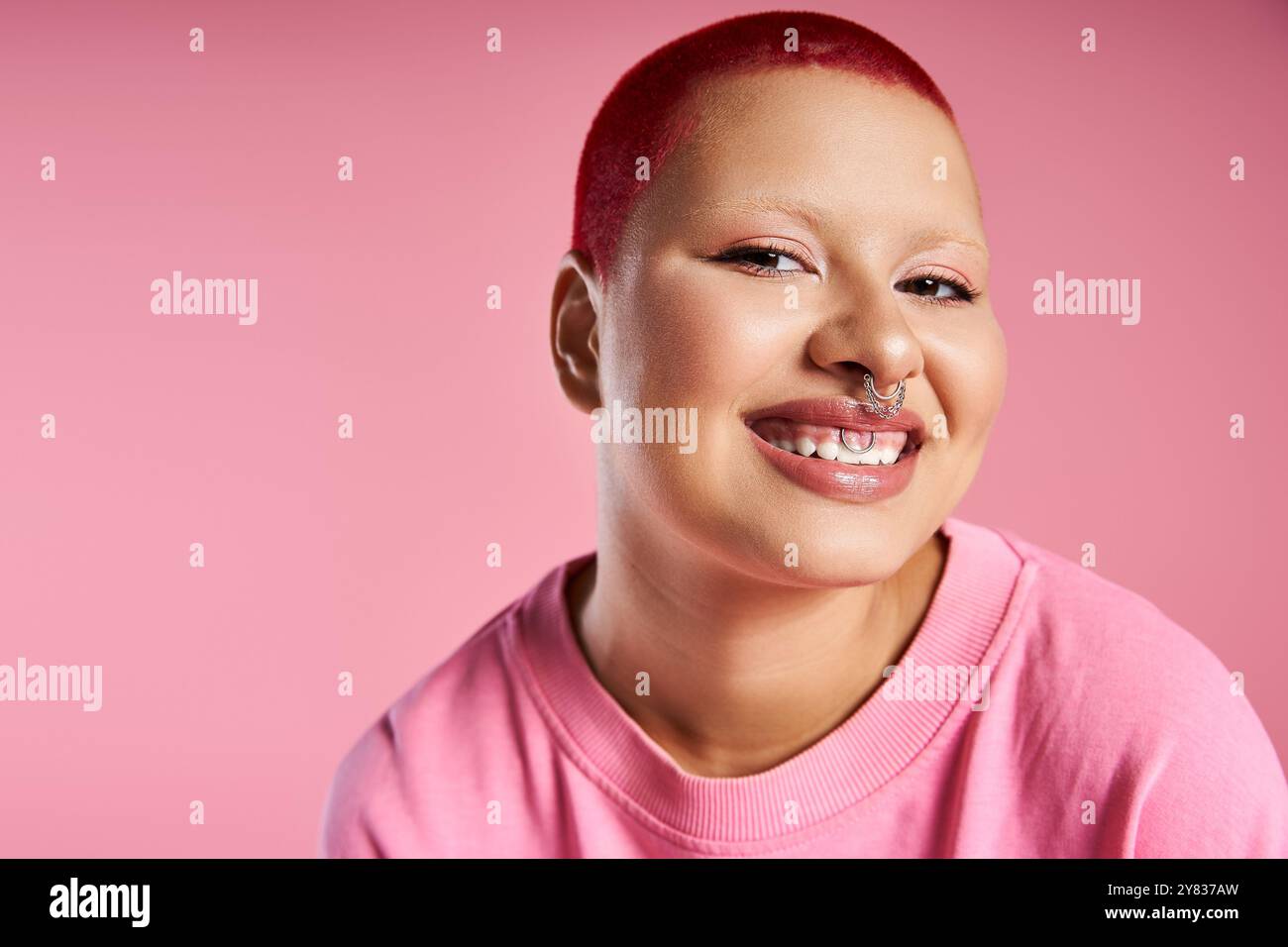 Diese selbstbewusste junge Frau mit rosa Haaren und einem Nasenstechen teilt ihre kühne Mode in einem farbenfrohen Studio. Stockfoto