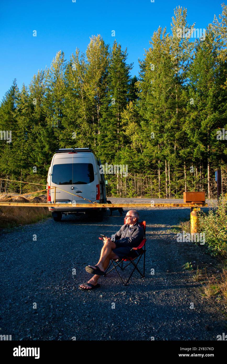 Ein älterer Mann, der sich an einer Straßensperre entspannt und ein Kindle-Buch liest. Mount Rainer National Park, Washington Stockfoto