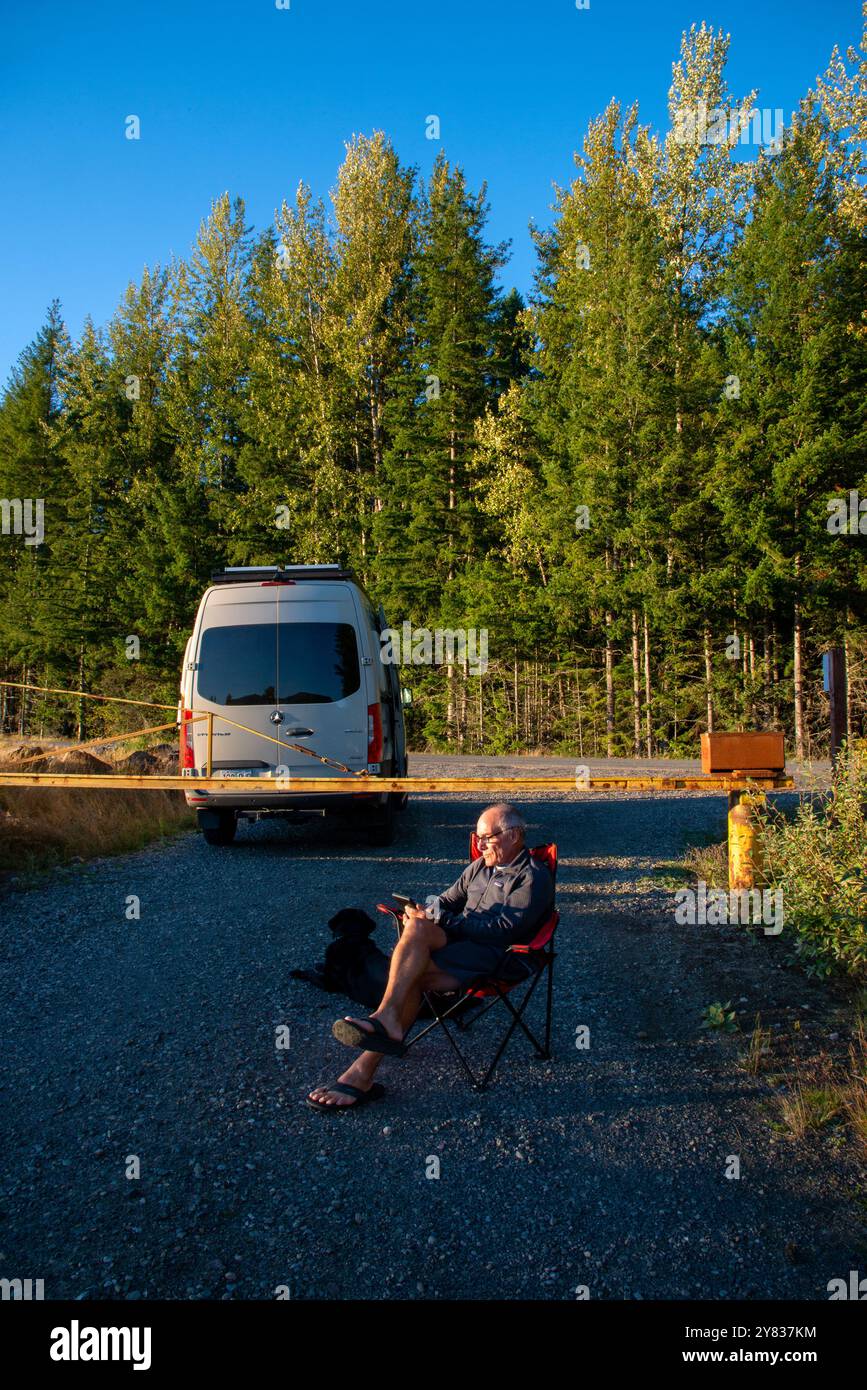 Ein älterer Mann, der sich an einer Straßensperre entspannt und ein Kindle-Buch liest. Mount Rainer National Park, Washington Stockfoto