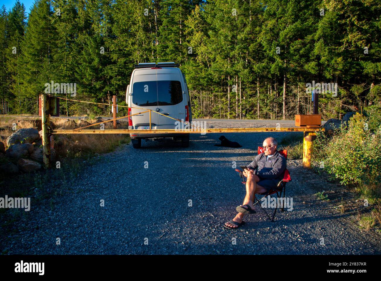 Ein älterer Mann, der sich an einer Straßensperre entspannt und ein Kindle-Buch liest. Mount Rainer National Park, Washington Stockfoto