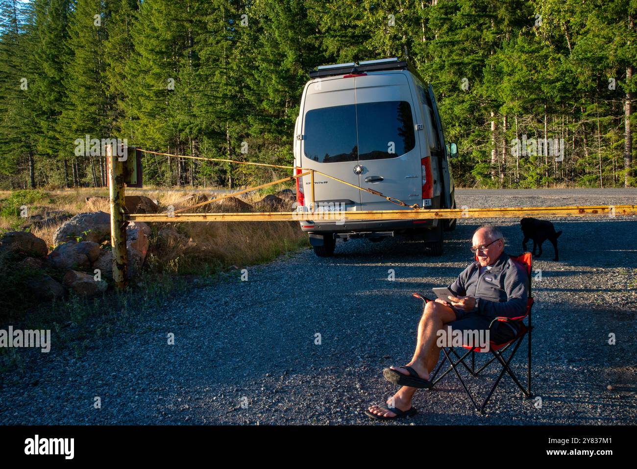 Ein älterer Mann, der sich an einer Straßensperre entspannt und ein Kindle-Buch liest. Mount Rainer National Park, Washington Stockfoto