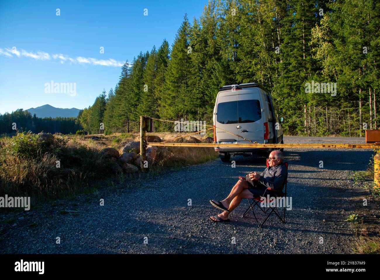 Ein älterer Mann, der sich an einer Straßensperre entspannt und ein Kindle-Buch liest. Mount Rainer National Park, Washington Stockfoto
