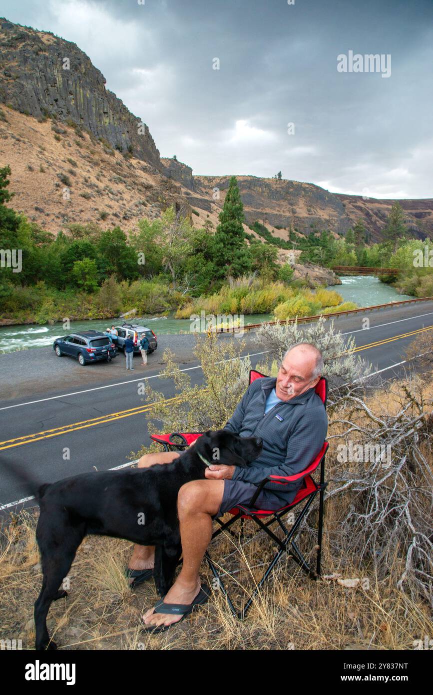 Ein Mann mit einem Senior entspannt sich mit seinem schwarzen Labor entlang des Highway 12 im Tieton River Canyon außerhalb von Yakima, Washington Stockfoto