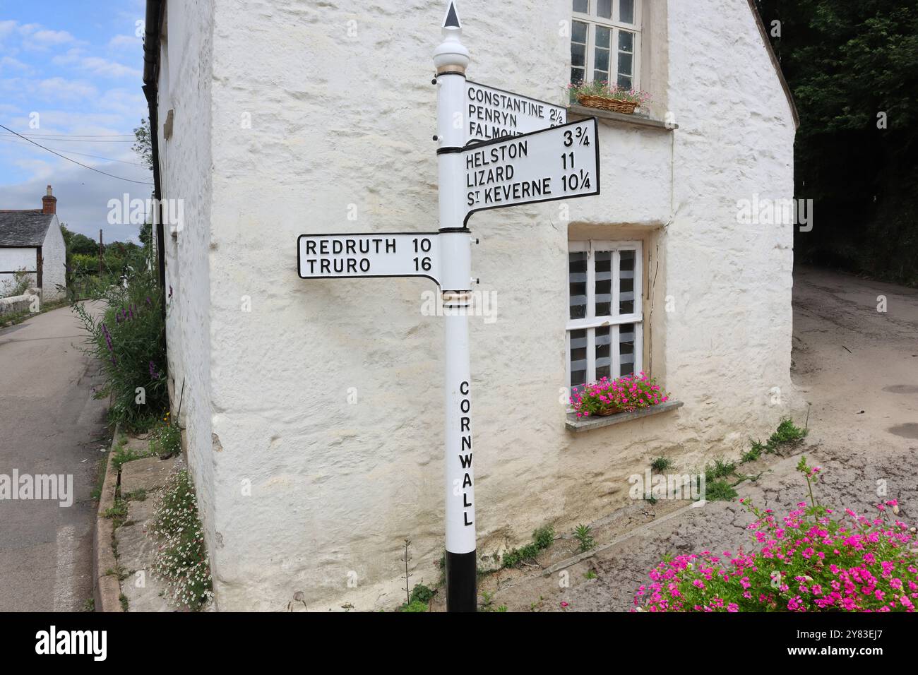 Ein altmodisches gusseisernes Schild führt Reisende zu berühmten Städten und Dörfern in Cornwall, mit der Kulisse eines typischen kornischen Ferienhauses Stockfoto