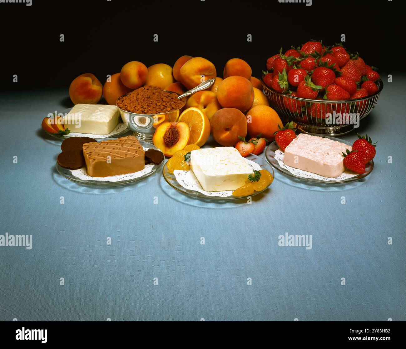 Verschiedene Frischkäsesorten mit Fruchtgeschmack, frische Erdbeeren, Aprikosen, Orangen mit Kuchen, Butter und braunem Zucker auf dem Tisch, buntes Stillleben Stockfoto
