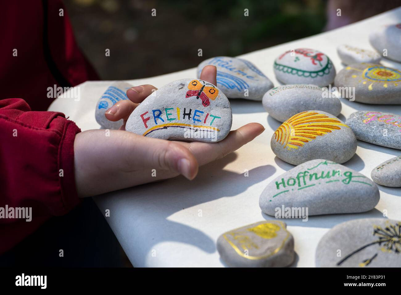 Sammlung von handgemalten Glückskies auf einem Tisch, Hand eines Kindes, das einen davon mit dem deutschen Wort Freiheit hält, was Freiheit bedeutet, kleine giveawa Stockfoto