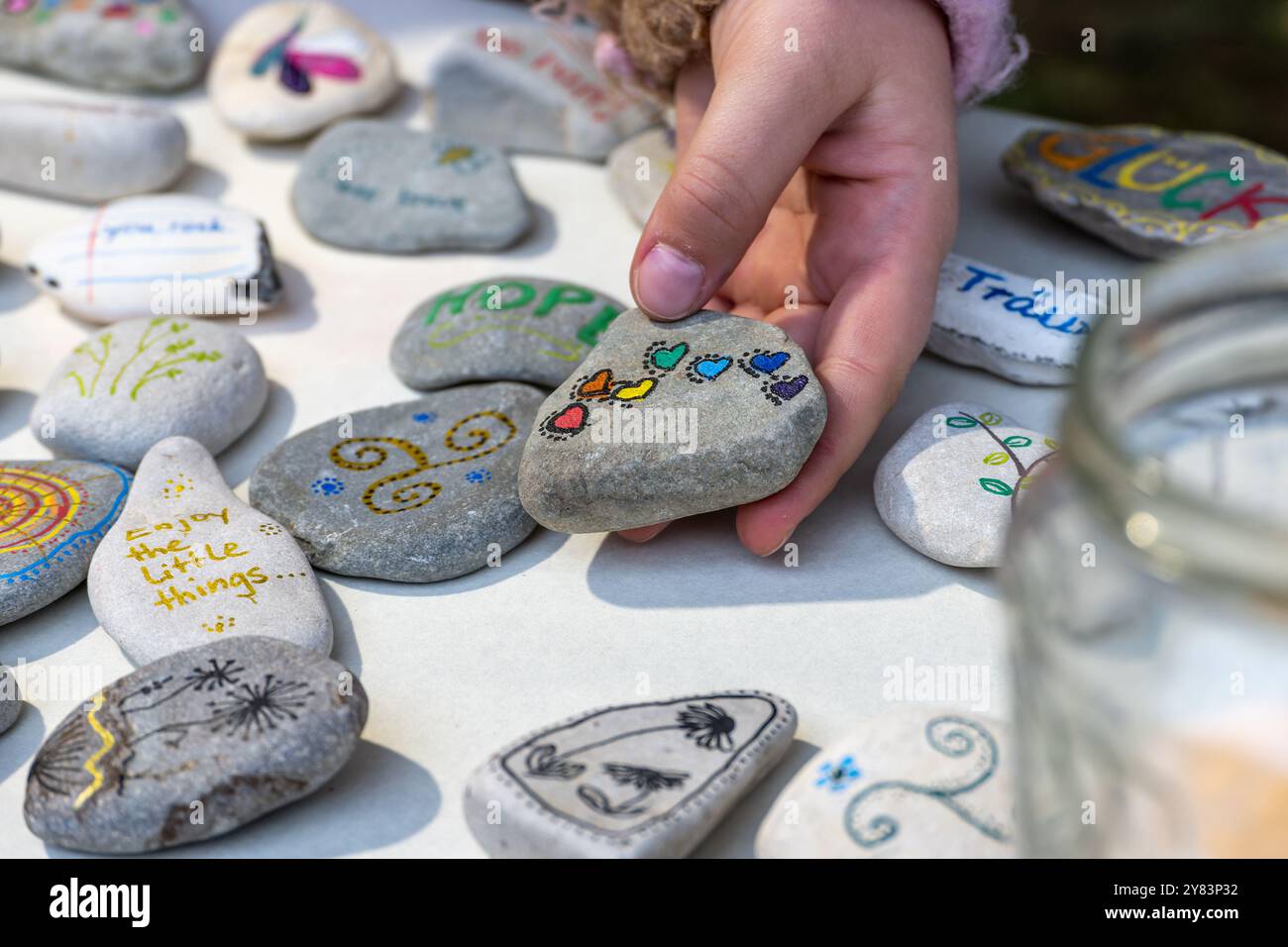 Sammlung von handbemalten Kieseln mit Symbolen, Hand eines Kindes, das einen davon mit dem Deutschen hält, mit bunten Herzen, kreative Geschenke zu machen Stockfoto
