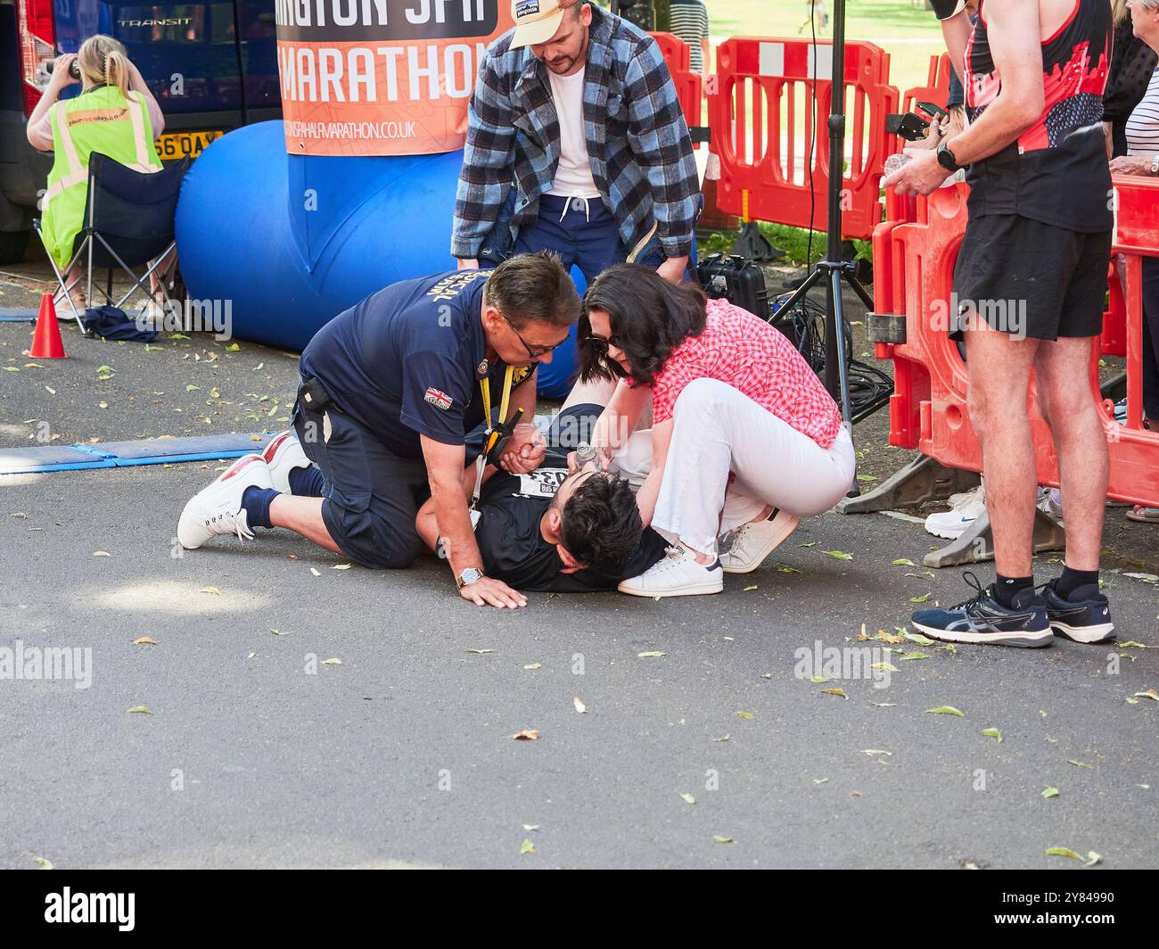 Kollabierender Halbmarathon-Läufer, der an der Ziellinie mit Hilfe eines Sanitäters behandelt wird. Stockfoto