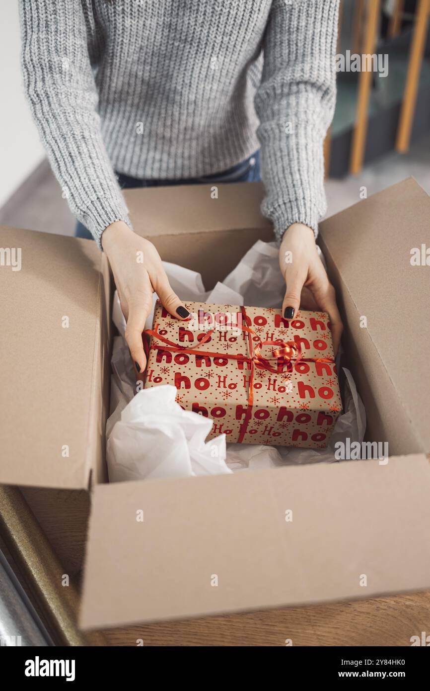Junge kaukasische Frau, die ein Geschenk einpackt und es für die Post bereit macht. Frau verpackt ein Überraschungsgeschenk für ein Familienmitglied, verpackt es in ein Stockfoto