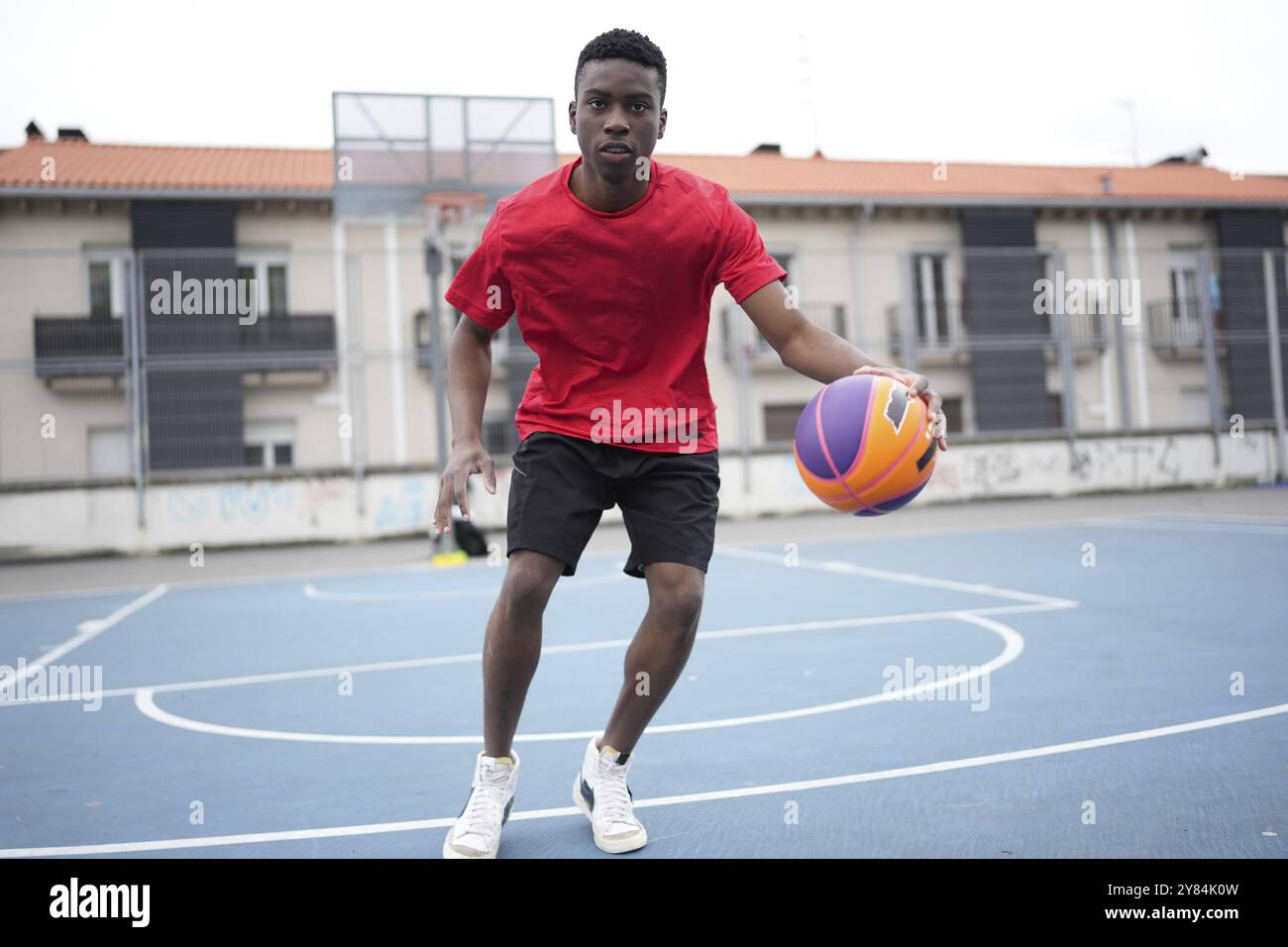 Frontales Foto von einem afrikanischen Basketballspieler, der auf einem Basketballfeld im Freien dribbelt Stockfoto