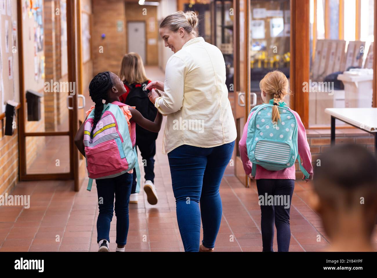 Im Schulflur spazieren, Lehrerin führt verschiedene Schüler mit Rucksäcken in den Unterricht Stockfoto