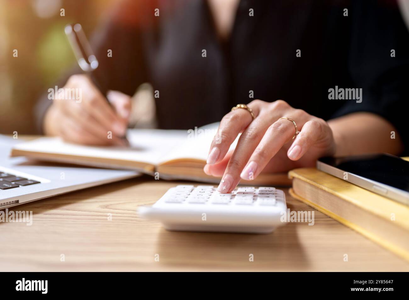 Eine Nahaufnahme einer Geschäftsfrau, die auf einen Taschenrechner klopft, während sie Notizen in einem Buch macht, an einem Tisch drinnen arbeitet. Finanzen, Buchhaltung, Budget Stockfoto