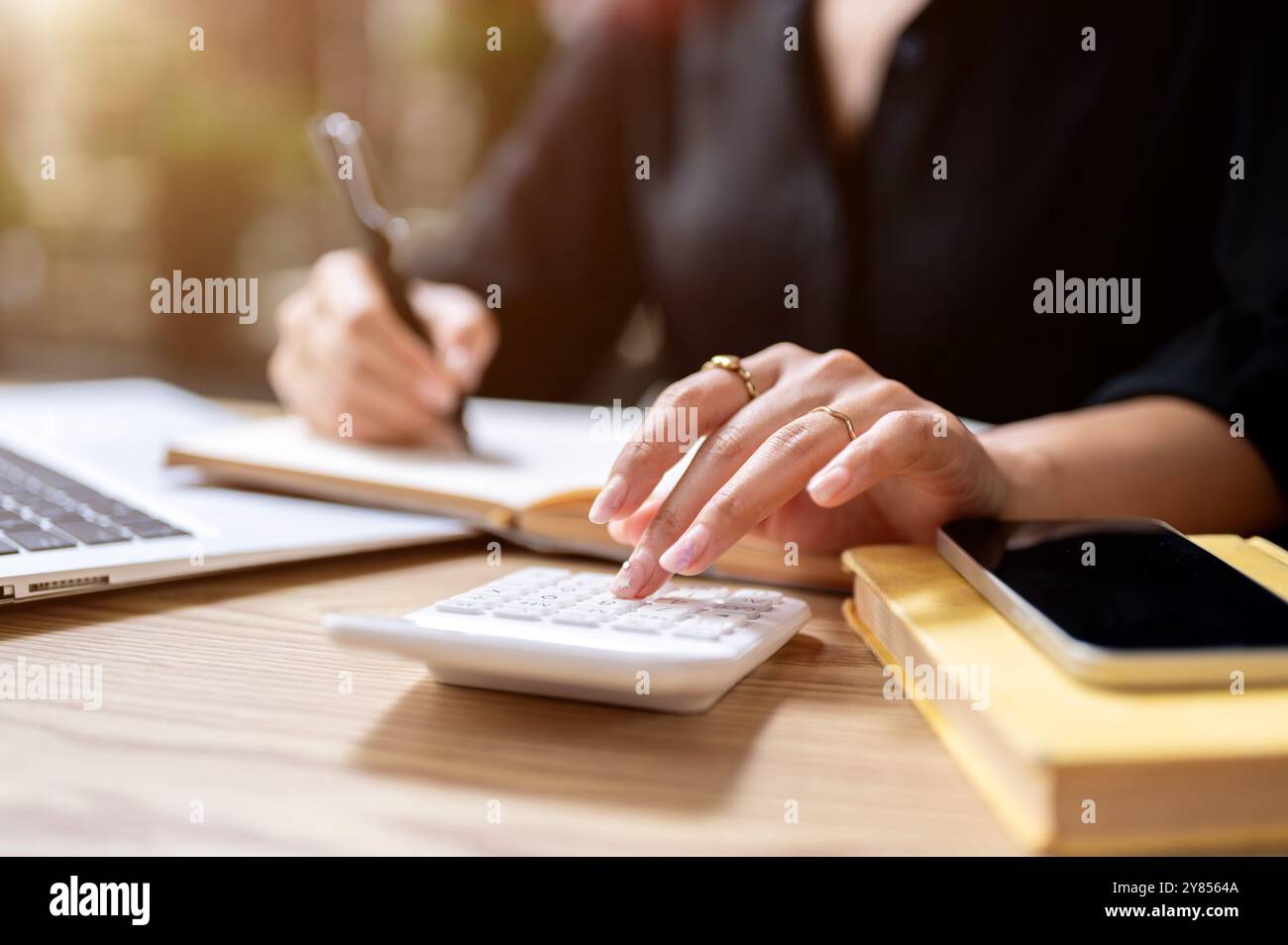 Eine Nahaufnahme einer Geschäftsfrau, die auf einen Taschenrechner klopft, während sie Notizen in einem Buch macht, an einem Tisch drinnen arbeitet. Finanzen, Buchhaltung, Budget Stockfoto