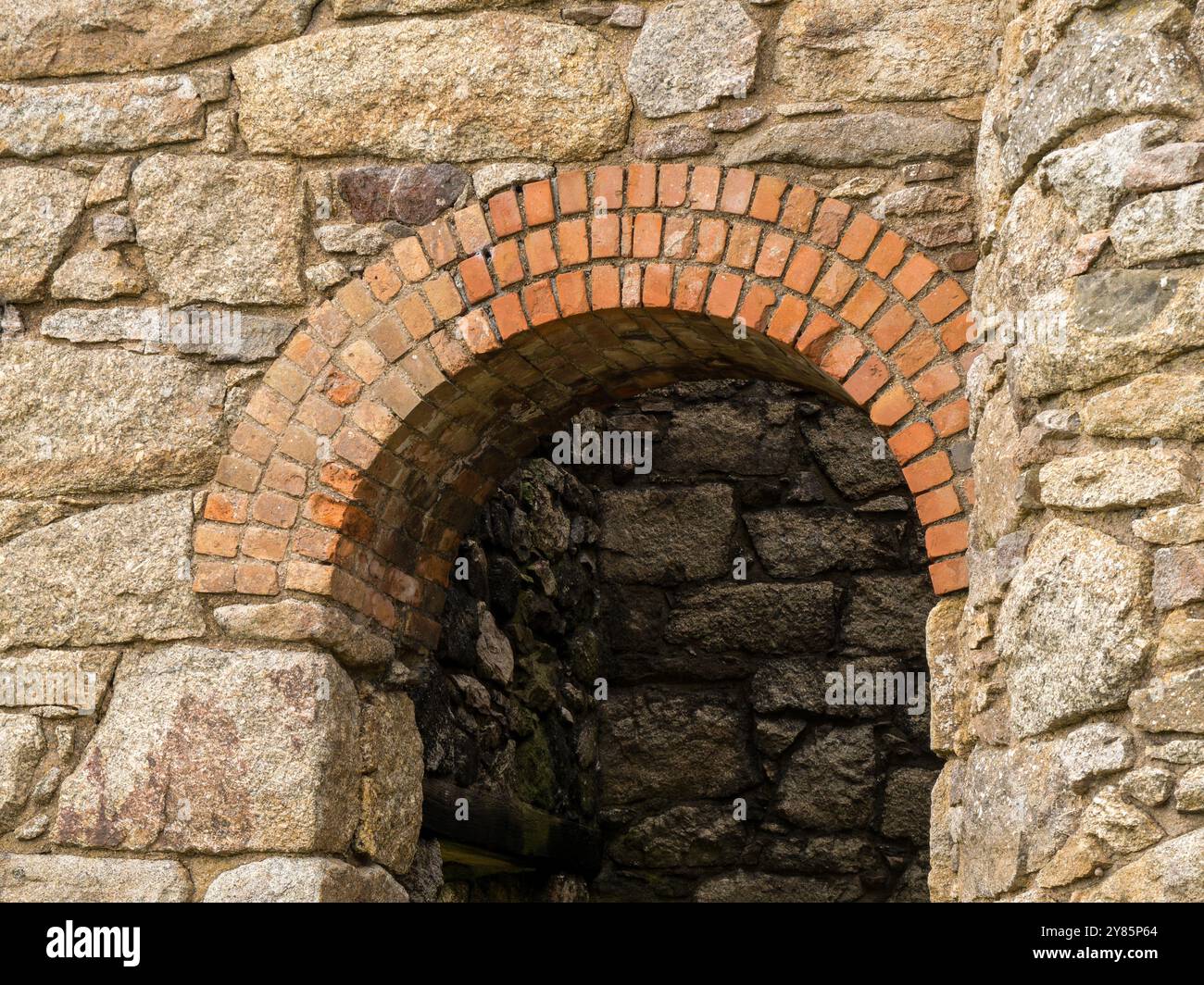 Römischer Bogen in der Mauer des alten kornischen Zinnbergwerks aus rotem Backstein und kornischem Granit, Botallack, Land’s End, Cornwall, England, UK. Stockfoto