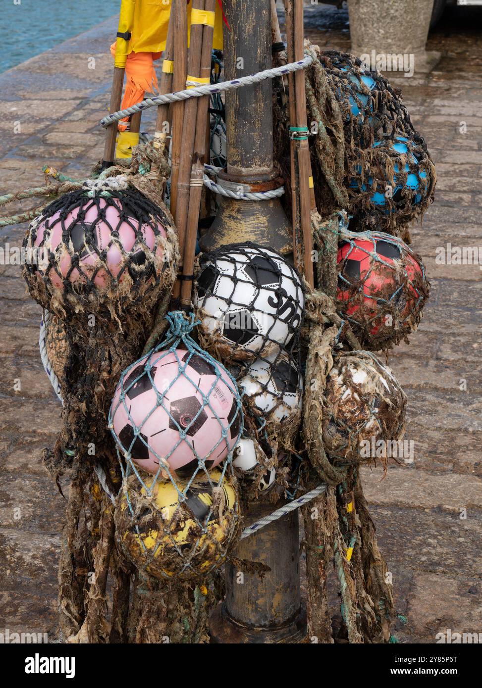 Eine Sammlung alter schwimmender Bojen für den Seefischer aus Plastikfußbällen und Netzgewebe, die am Ufer des St. Ives Harbour in Cornwall, England, Großbritannien, hängen Stockfoto