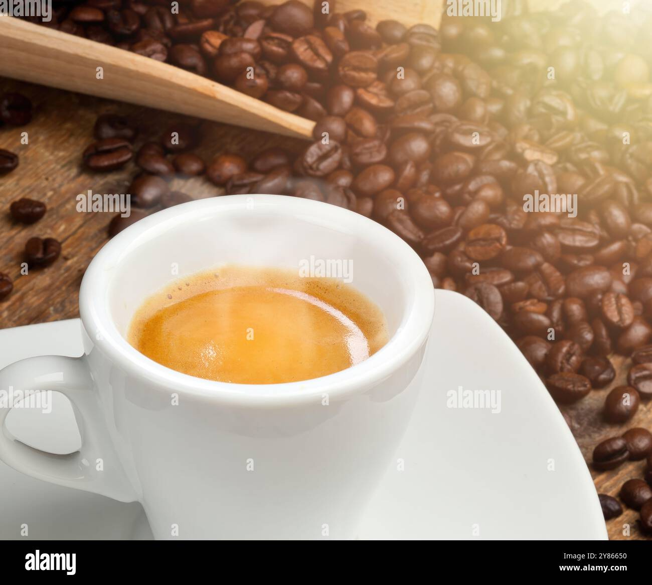 Dampfender Espresso-Kaffee in weißer Tasse auf Untertasse mit Kaffeebohnen in Holzlöffel auf rustikalem Holzhintergrund Stockfoto