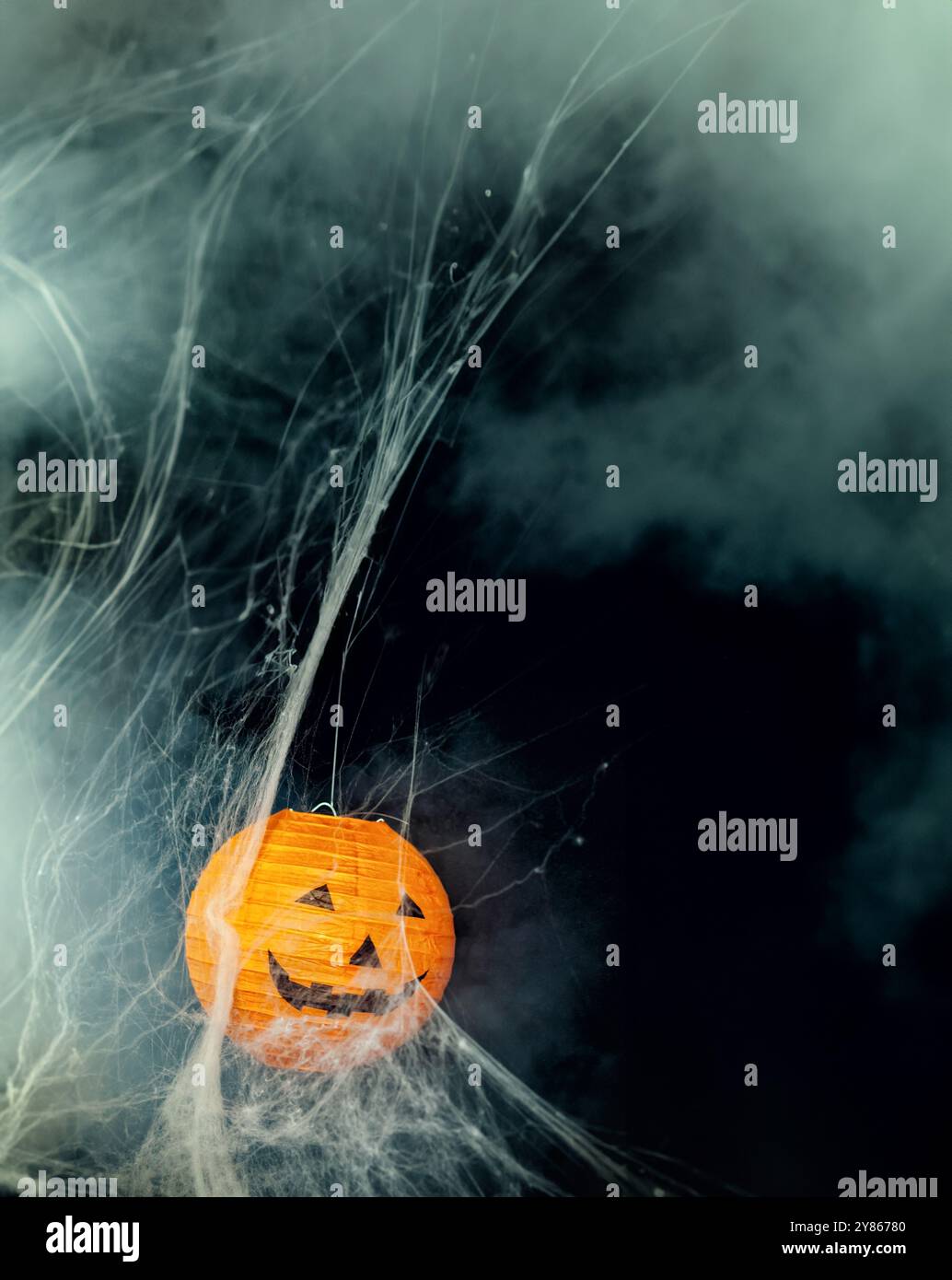 Halloween-Kürbislaterne, die im Nebel und im Spinnweben leuchtet, schafft eine gruselige Atmosphäre für eine festliche Feier Stockfoto