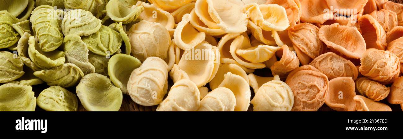Bunte, ungekochte Orecchiette-Nudeln in Grün, weiß und Orange. Perfekt für Liebhaber der mediterranen Küche. Geschmacksverstärker für jede Diät Stockfoto