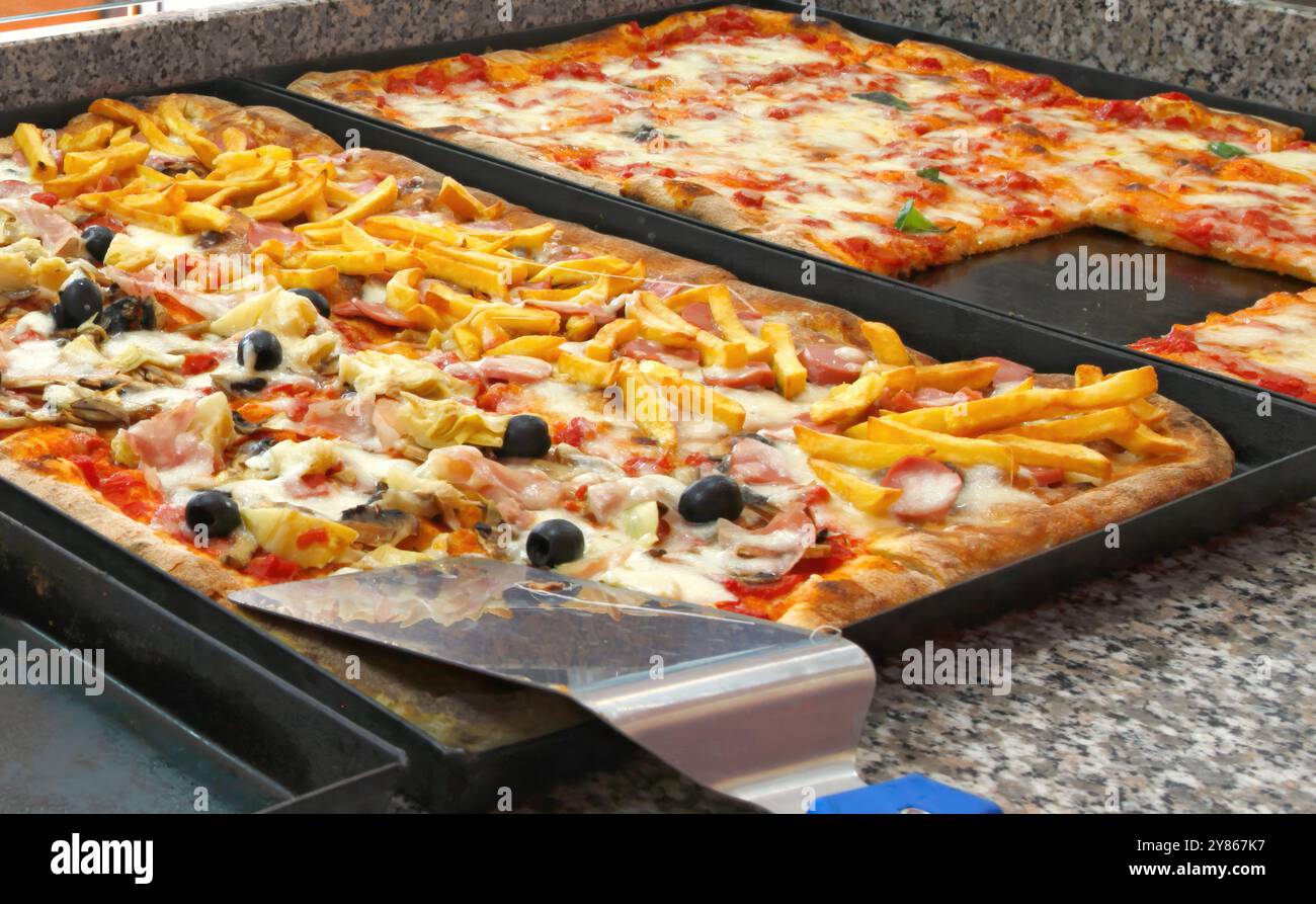 Frisch gebackene Pizzen mit geschmolzenem Mozzarella-Käse und verschiedenen Belägen warten darauf, in einer Pizzeria serviert zu werden Stockfoto