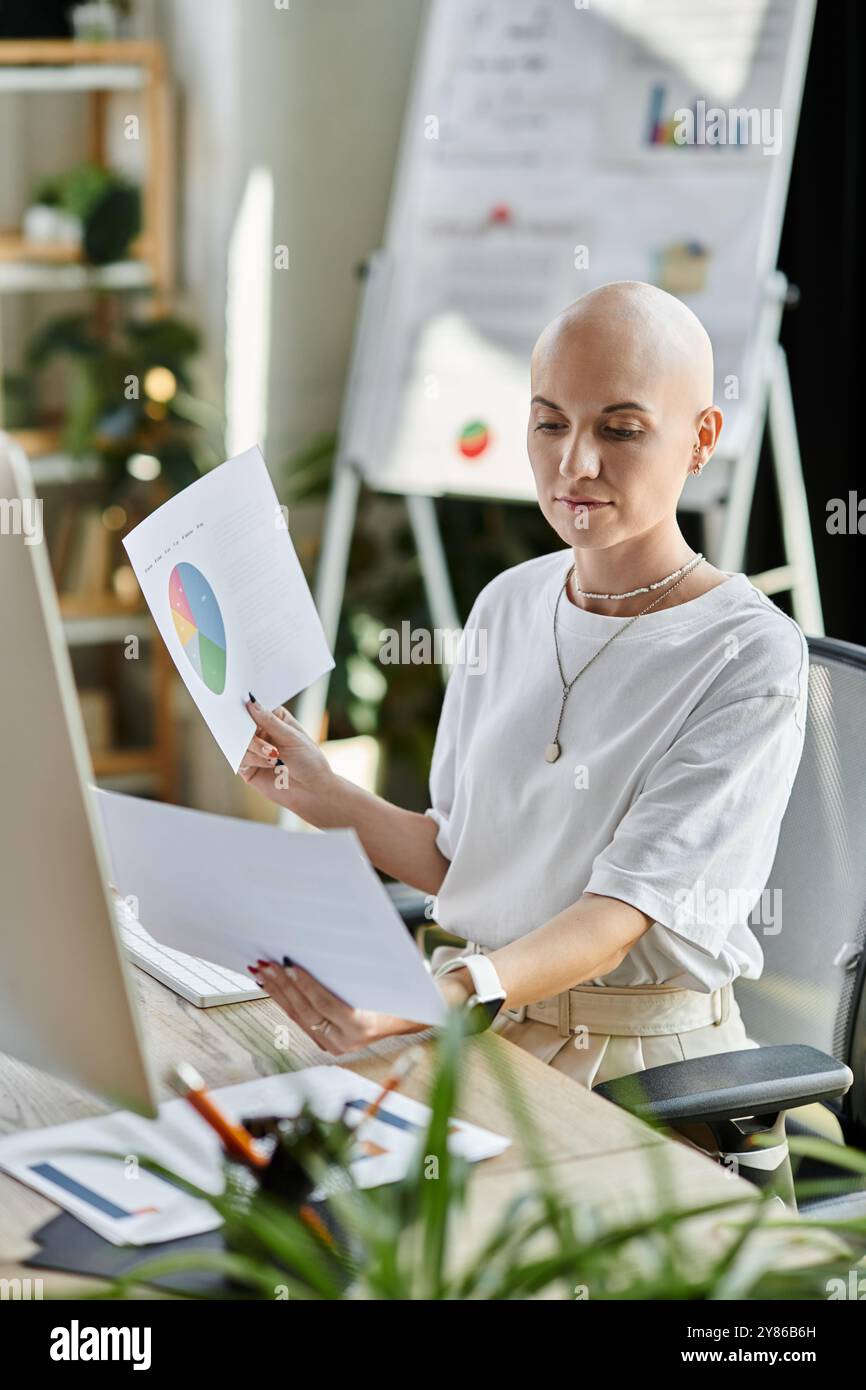 Eine junge kahlköpfige Frau studiert tagsüber detaillierte Berichte und Diagramme an ihrem eleganten Arbeitsplatz. Stockfoto