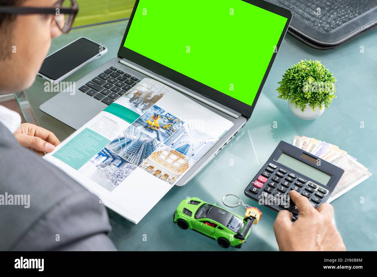 Ein fokussierter Geschäftsmann sitzt an einem eleganten, modernen Schreibtisch und berechnet seine monatlichen EMI-Zahlungen für verschiedene Arten von Krediten, darunter Auto, Haus, Geschäft Stockfoto