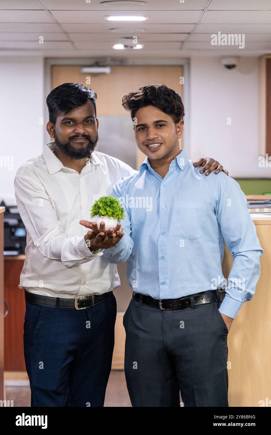 Zwei männliche Kollegen posieren in einem modernen Büro, halten stilvolle Pflanzenpräsentation, freundlichen Ausdruck und moderne Arbeitsraumeinrichtung Stockfoto